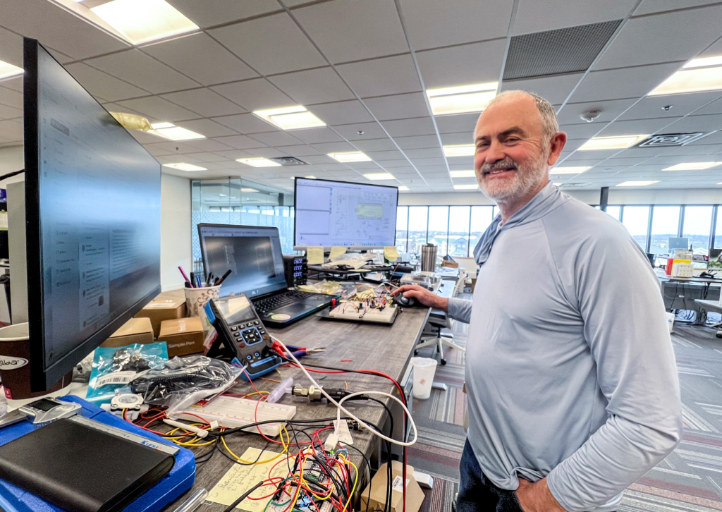 Man standing at computer desk with mechanics for a pump.